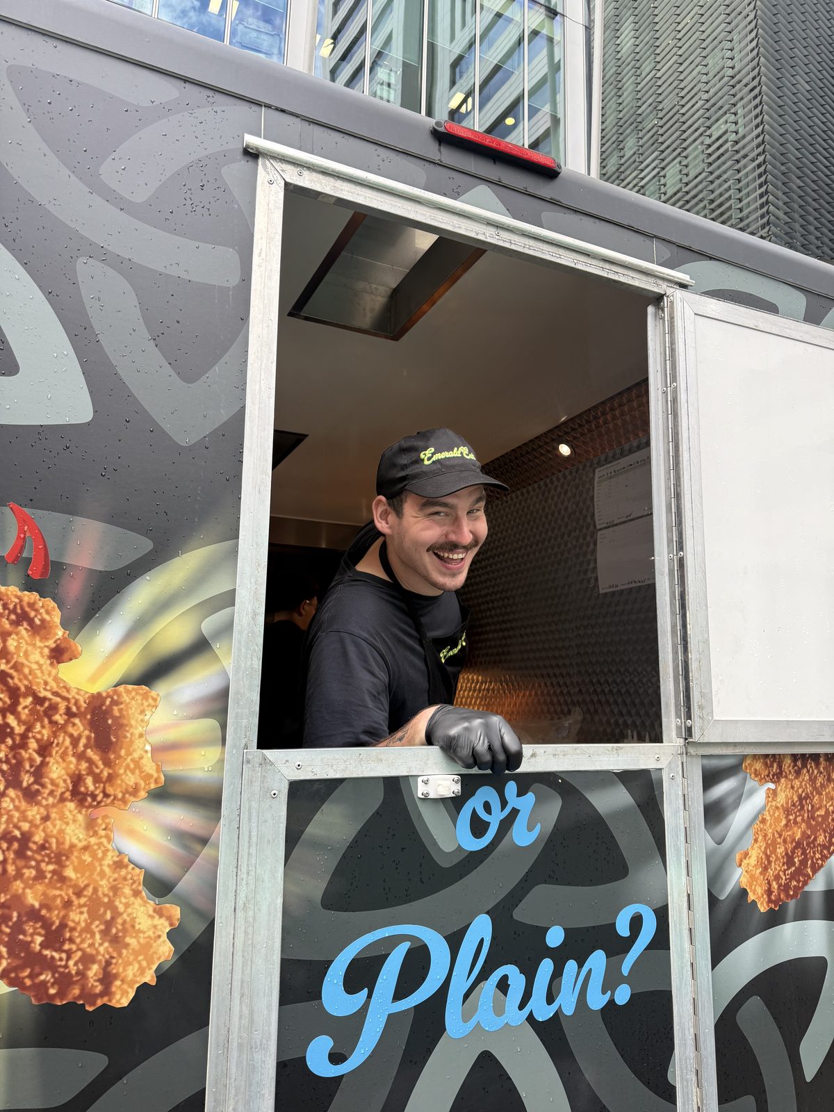 Street food trader leaning out of a hatch in a graphic-wrapped food truck